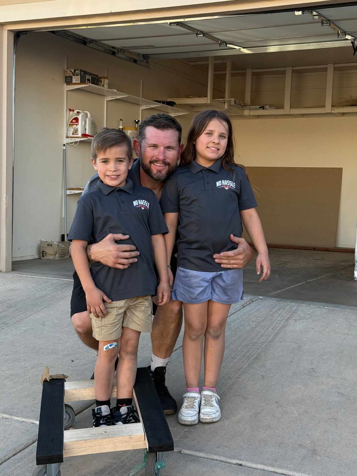 Sam, founder of No Hassle Movers, with his two children in company shirts at the family-owned Tucson moving business